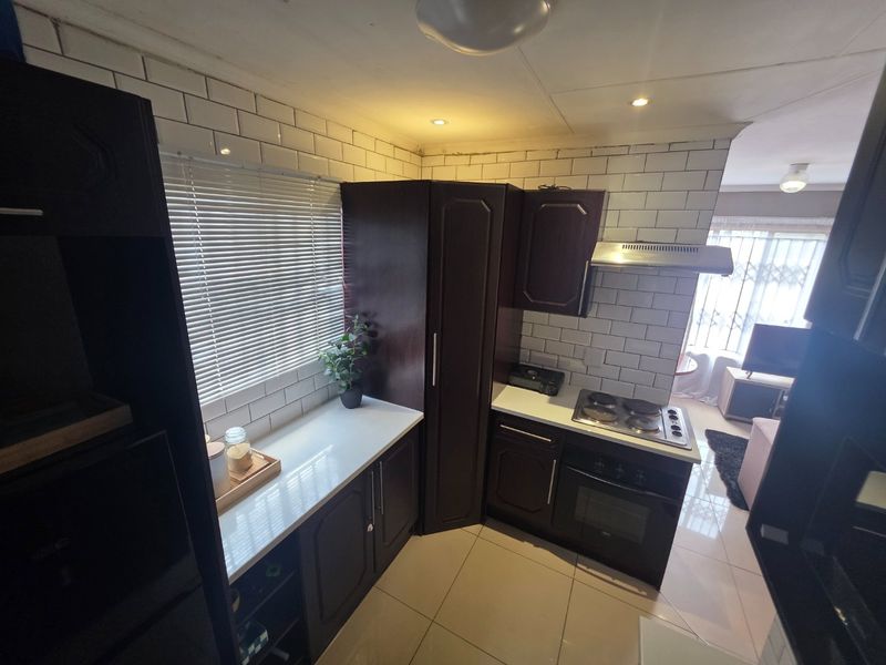 Compact kitchen featuring dark wood cabinetry, white subway tile backsplash, built-in oven, and electric hob, with an open-plan flow to the living area.