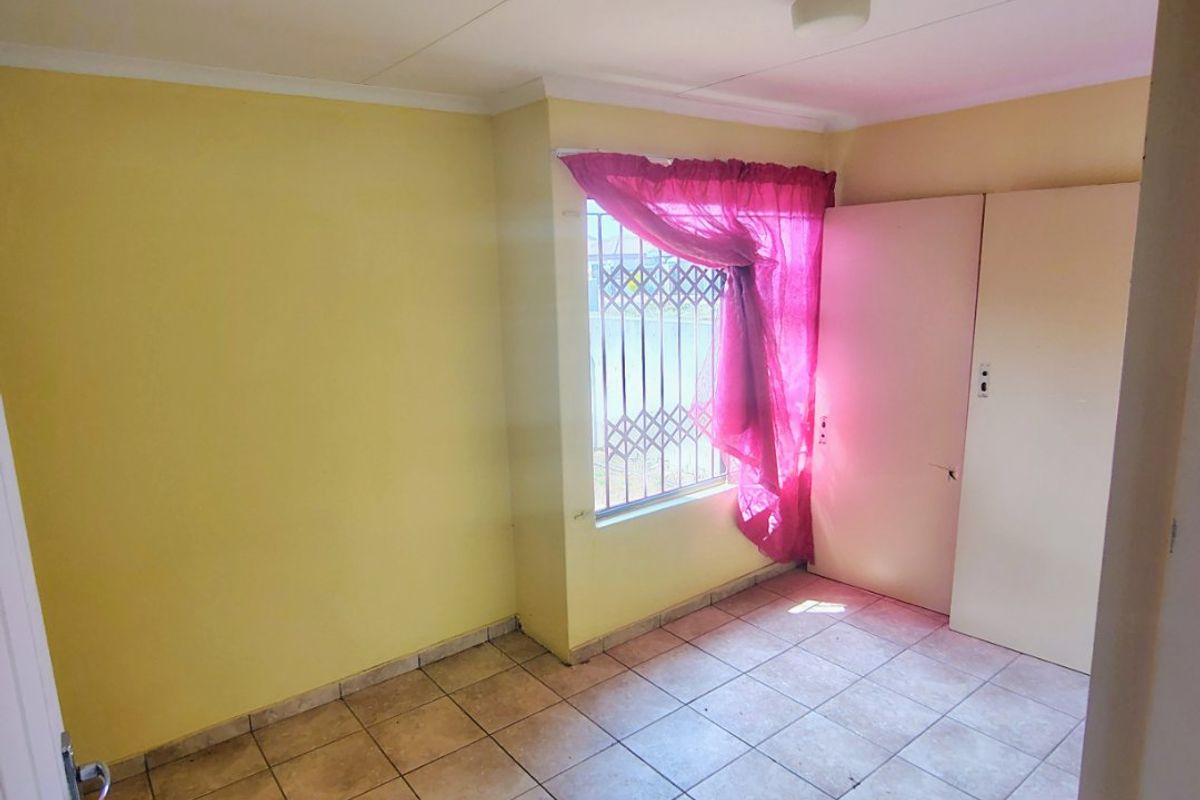 An empty bedroom featuring tiled flooring, built-in cupboards, and security bars on the window, offering a blank canvas for renovation.