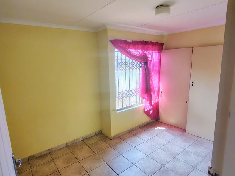 An empty bedroom featuring tiled flooring, built-in cupboards, and security bars on the window, offering a blank canvas for renovation.