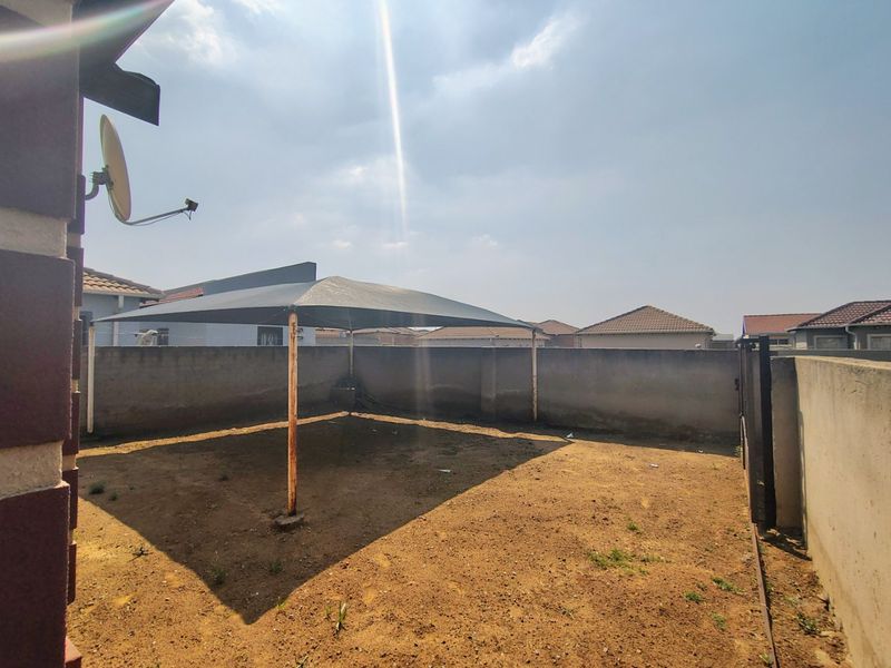 A rear yard area featuring a perimeter boundary wall and a central shade sail structure over an unlandscaped ground surface.