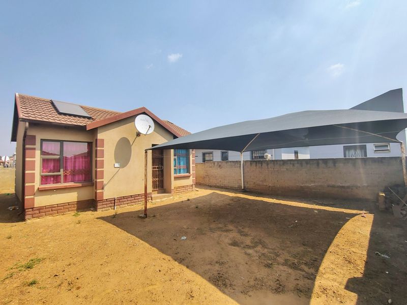 Rear exterior view of the house featuring a tiled roof with solar geyser, security gates, and a large shade sail covering the yard area.