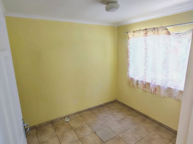 An empty bedroom featuring yellow walls, tiled flooring, and a ceiling-mounted light fixture, offering a blank canvas for potential updates.