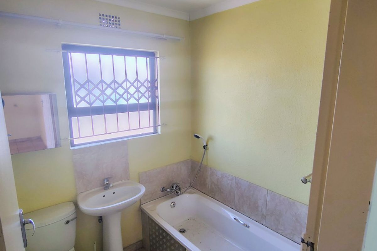 A compact bathroom featuring a pedestal basin, bathtub with shower mixer, and toilet, requiring cosmetic updates to the finishes and flooring.