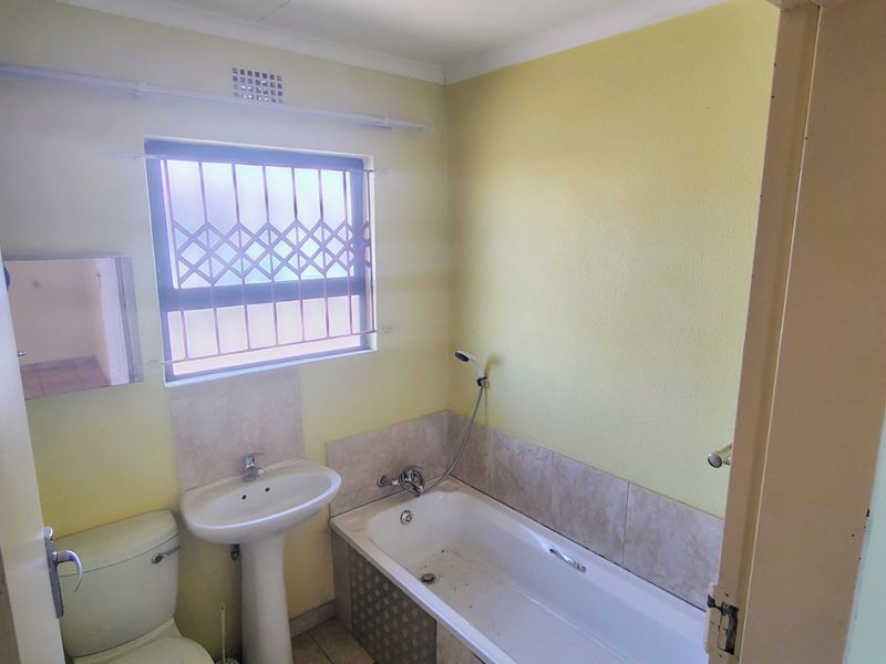 A compact bathroom featuring a pedestal basin, bathtub with shower mixer, and toilet, requiring cosmetic updates to the finishes and flooring.