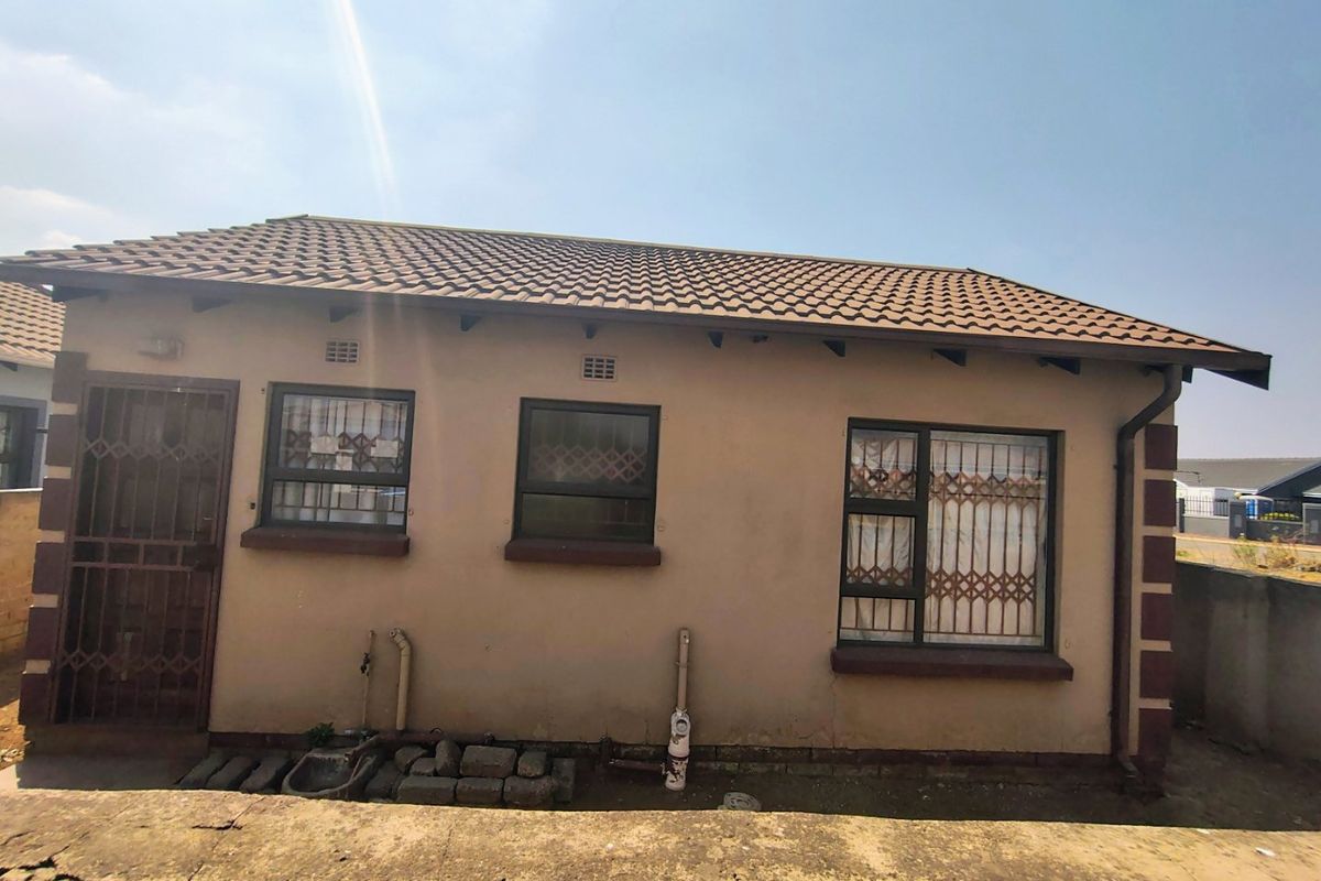 Rear exterior view of the house featuring a tiled roof, security gates, and aluminium window frames with visible exterior plumbing.