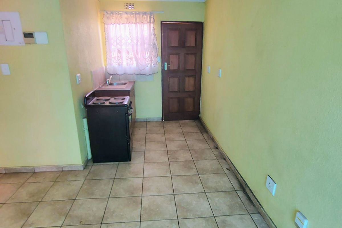 A compact, empty kitchen area featuring tiled flooring, a built-in sink, and direct access to an exterior door.