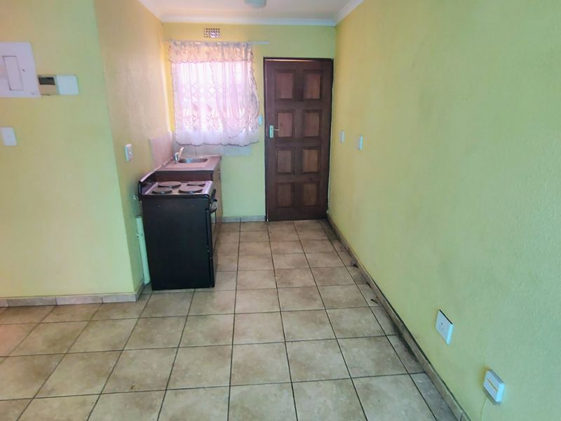 A compact, empty kitchen area featuring tiled flooring, a built-in sink, and direct access to an exterior door.