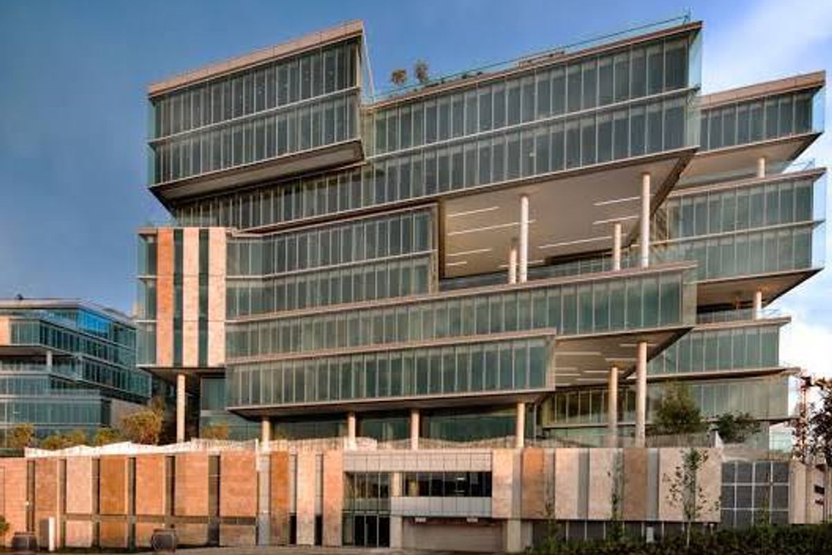 Modern commercial office building featuring a striking glass curtain wall facade, cantilevered levels, and stone-clad base with integrated parking access.