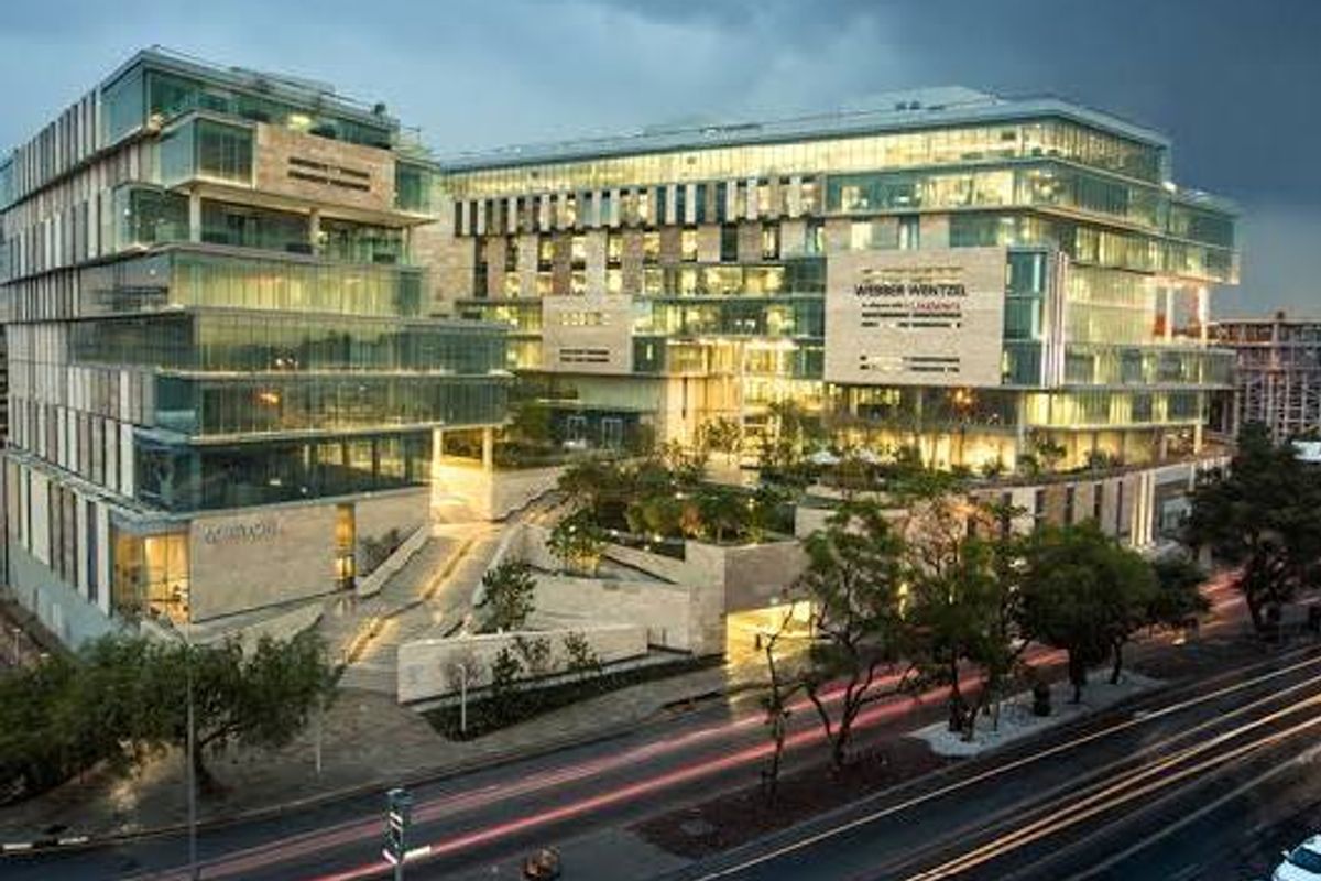 A modern commercial office complex featuring glass curtain walls, stone cladding, and integrated landscaped terraces at dusk.