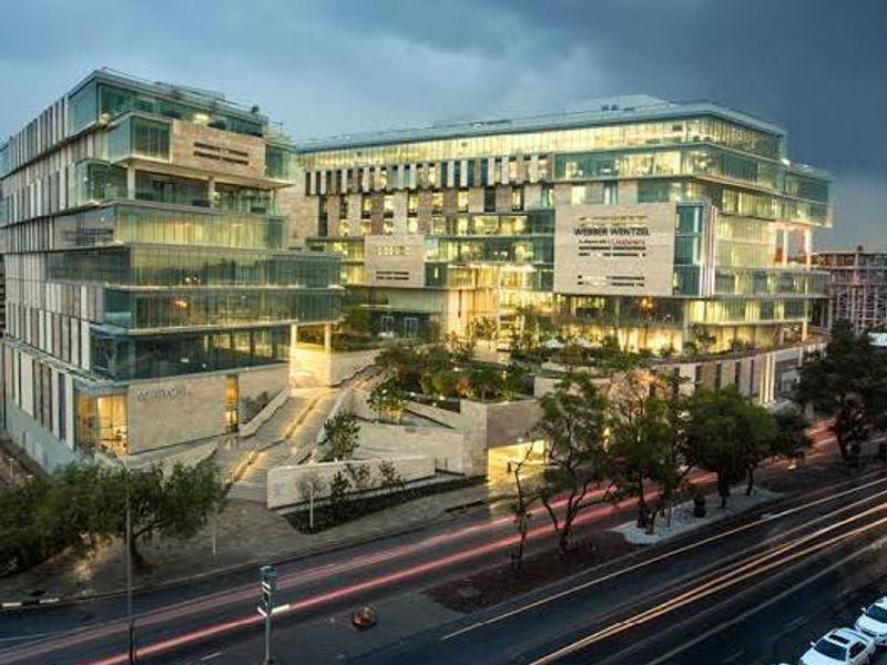 A modern commercial office complex featuring glass curtain walls, stone cladding, and integrated landscaped terraces at dusk.