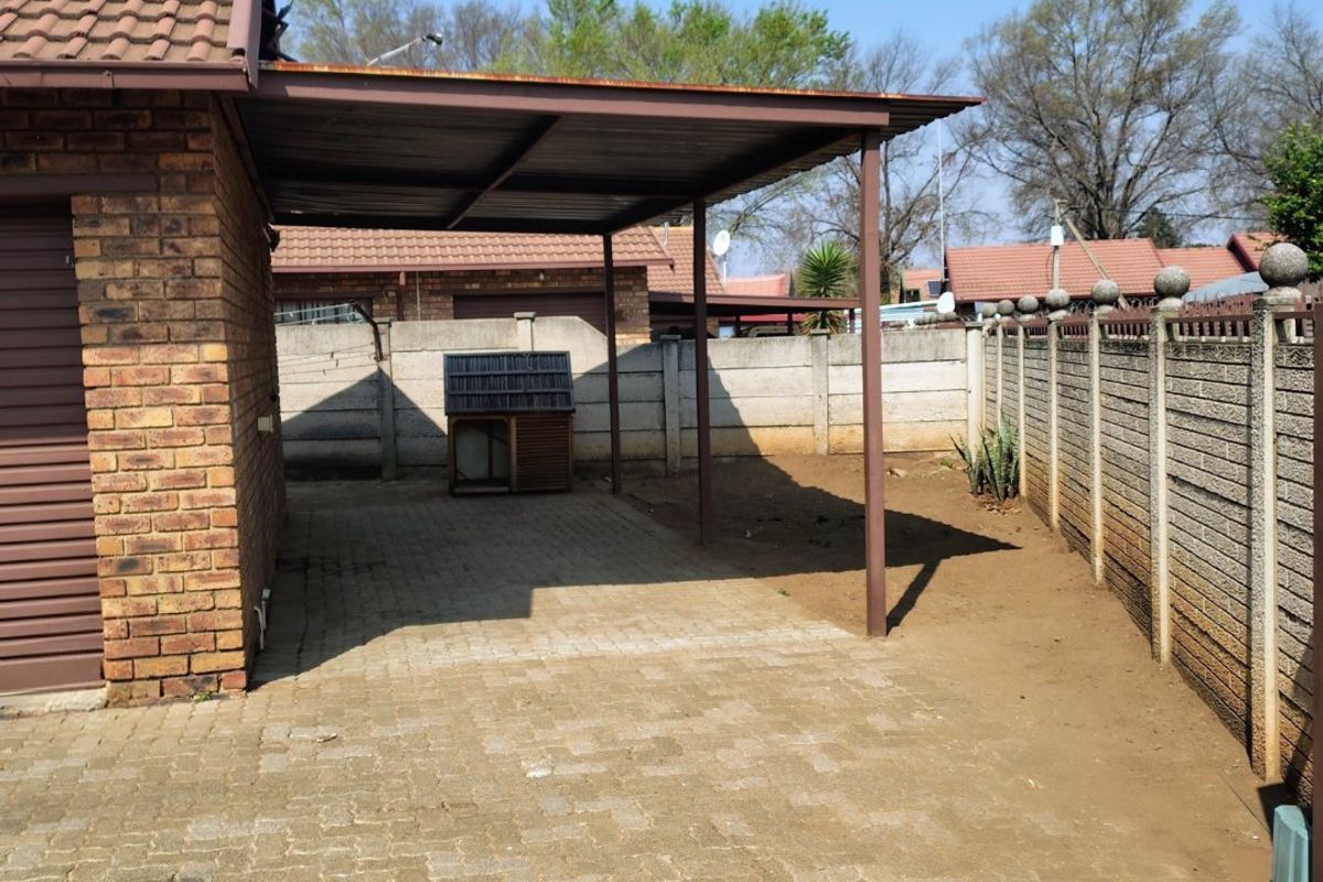 A paved rear yard area featuring a covered carport structure, enclosed by precast concrete perimeter walls.