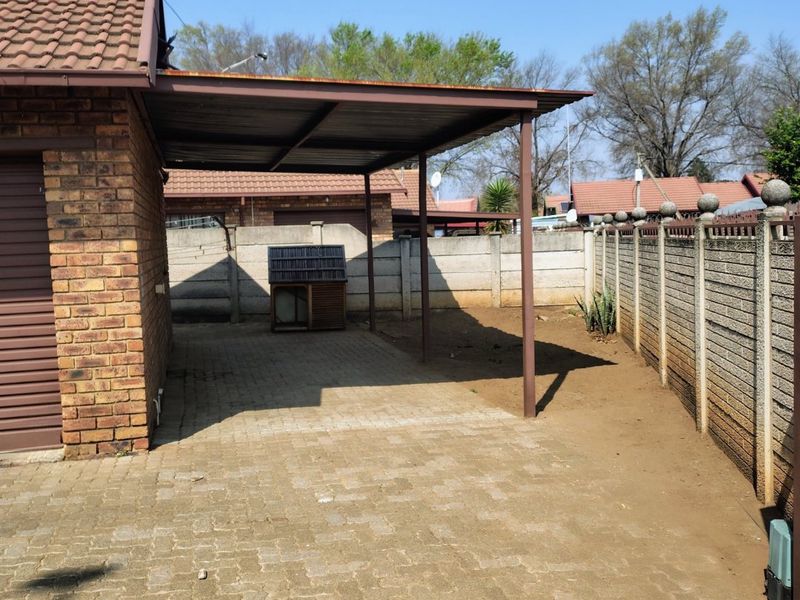 A paved rear yard area featuring a covered carport structure, enclosed by precast concrete perimeter walls.