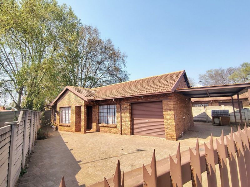 Front view of a face brick house featuring a paved driveway, single garage with roller door, carport, and secure boundary walling.
