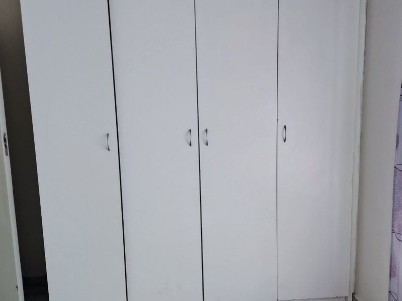 A bedroom featuring white built-in wardrobes and neutral tiled flooring, providing a clean and functional storage solution.
