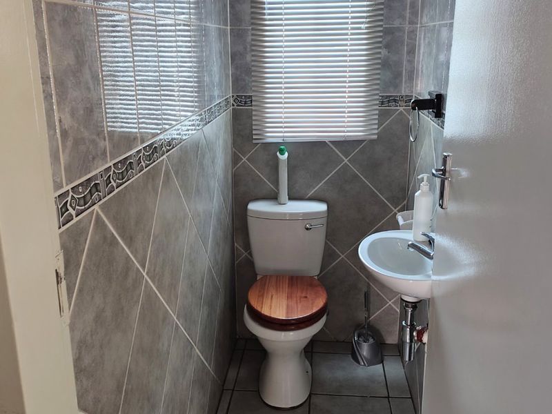 A compact guest bathroom featuring full-height ceramic wall tiling, a wall-mounted basin, and a standard toilet.