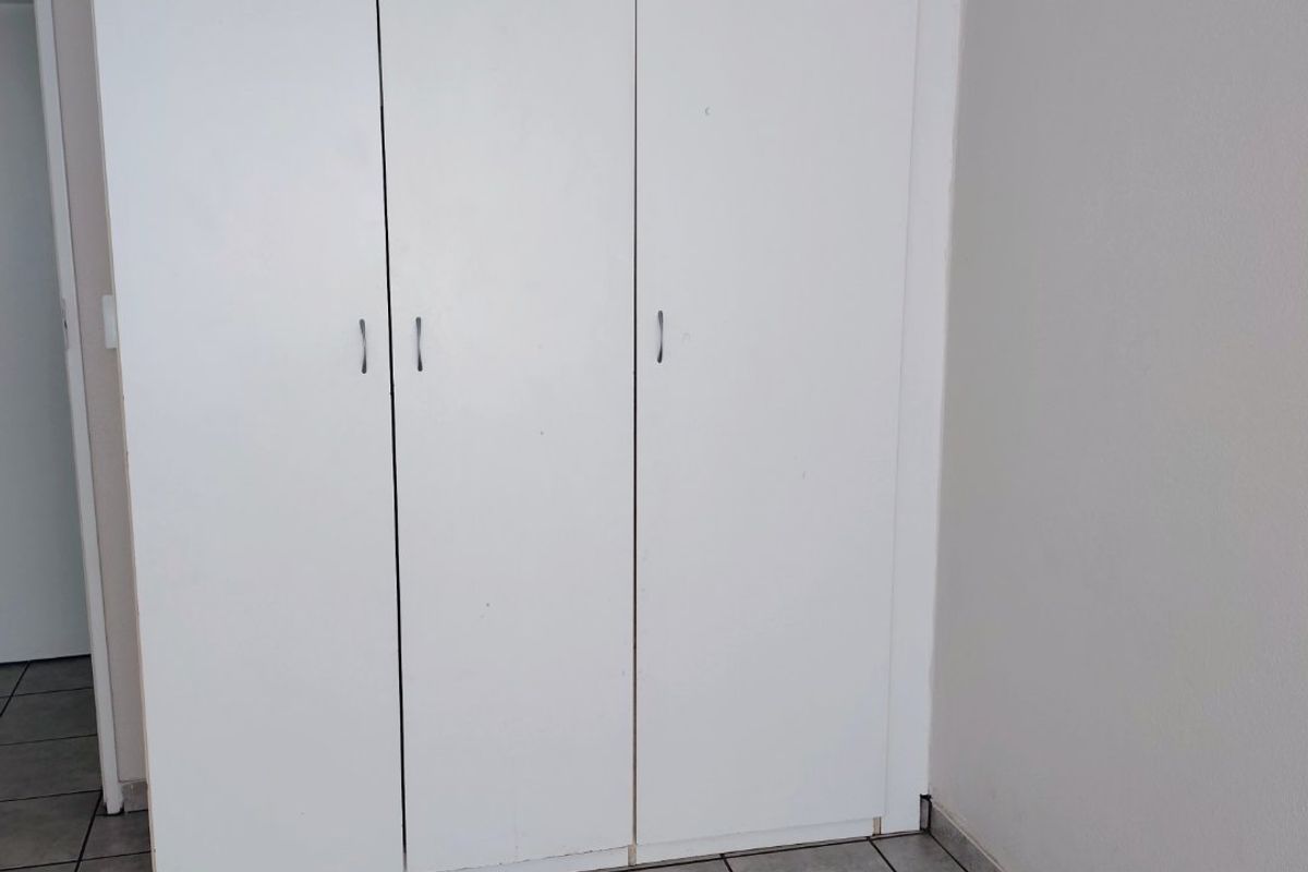 A clean, empty bedroom featuring neutral tiled flooring and a functional white built-in wardrobe with three doors.