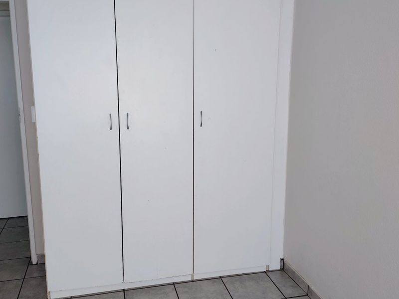 A clean, empty bedroom featuring neutral tiled flooring and a functional white built-in wardrobe with three doors.