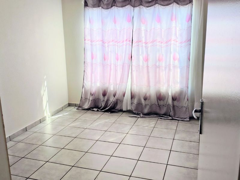 A bright, empty bedroom featuring neutral tiled flooring and a curtain rod, offering a clean canvas for personalization.