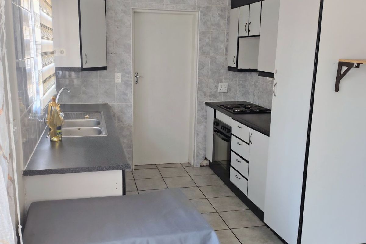 Functional kitchen featuring built-in cabinetry, laminate countertops, a stainless steel sink, and integrated oven with gas hob, finished with ceramic wall and floor tiles.