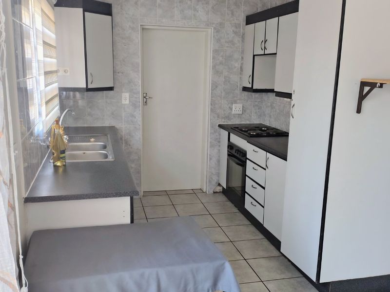 Functional kitchen featuring built-in cabinetry, laminate countertops, a stainless steel sink, and integrated oven with gas hob, finished with ceramic wall and floor tiles.