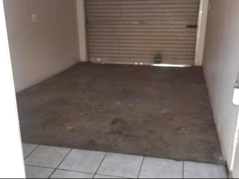 An empty garage space featuring a roller shutter door and a combination of tiled and concrete flooring.