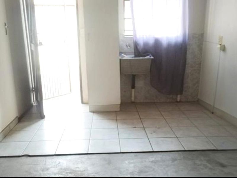 A functional laundry area featuring tiled flooring, a wall-mounted utility sink, and direct access to the exterior via a security gate.