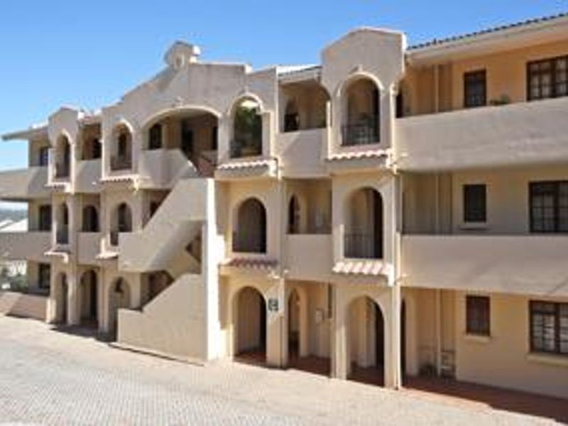 Exterior view of a multi-story apartment complex featuring arched balconies, stucco facade, and an external staircase.