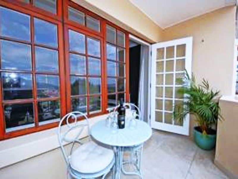A covered balcony featuring timber-framed windows and classic french doors, providing a pleasant outdoor space with tiled flooring.