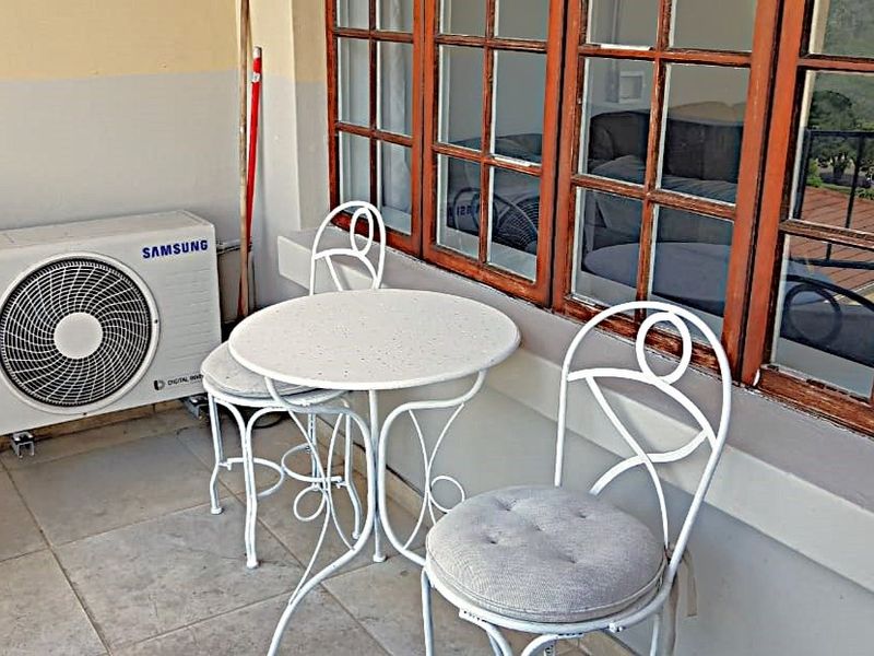 A compact balcony area featuring tiled flooring, a wall-mounted air conditioning unit, and timber-framed windows looking into the apartment interior.
