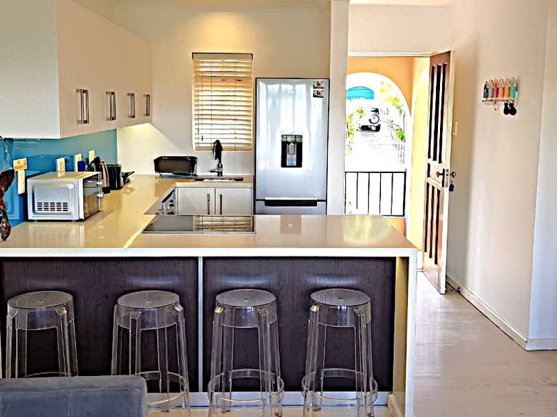 Modern kitchen featuring sleek white cabinetry, stone countertops, an integrated electric hob, and a breakfast bar, leading to an outdoor balcony area.