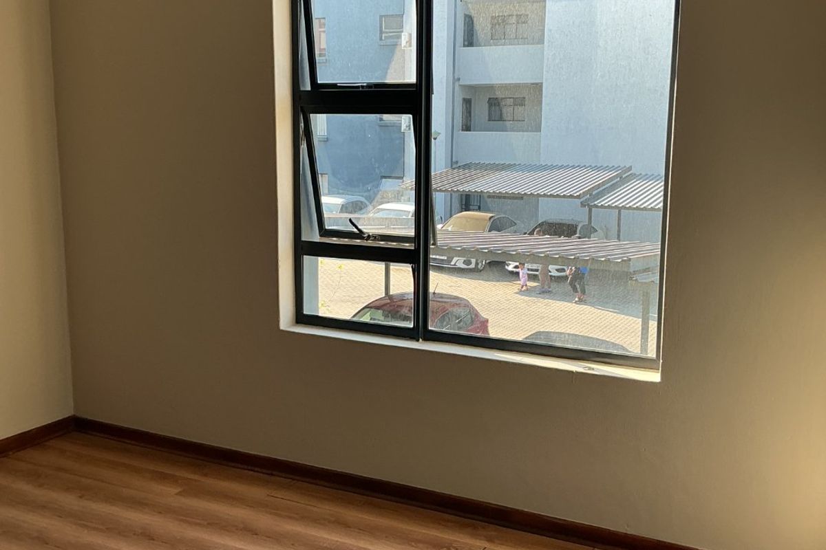 An empty bedroom featuring laminate flooring, neutral wall paint, and an aluminium window frame with an installed curtain rod.
