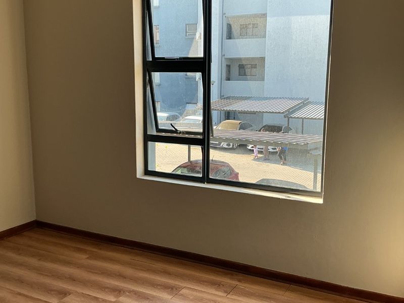 An empty bedroom featuring laminate flooring, neutral wall paint, and an aluminium window frame with an installed curtain rod.