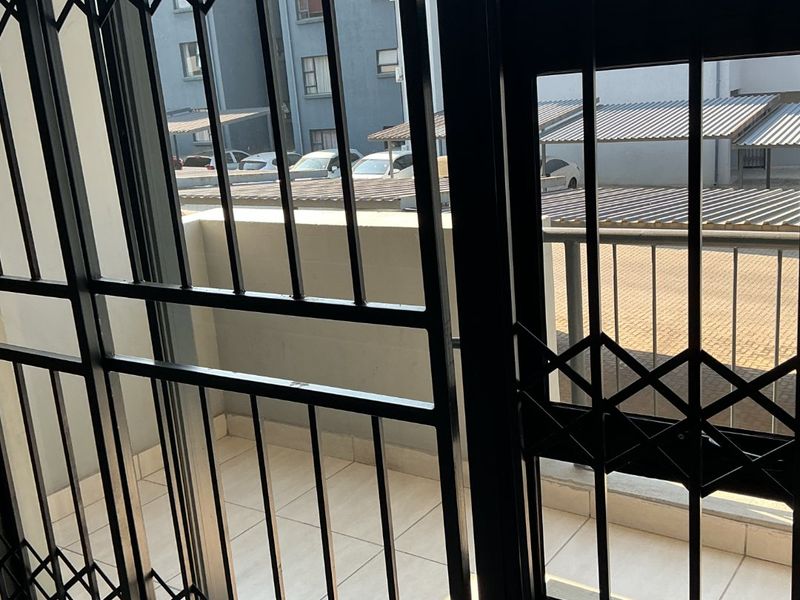 A tiled balcony area featuring a black metal security gate and railing, overlooking the apartment complex parking area.