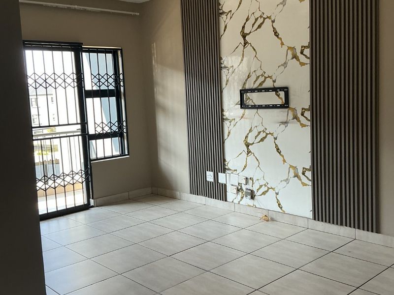 A bright, empty living room featuring modern marble-effect wall paneling, vertical timber slats, tiled flooring, and a secure entrance door.