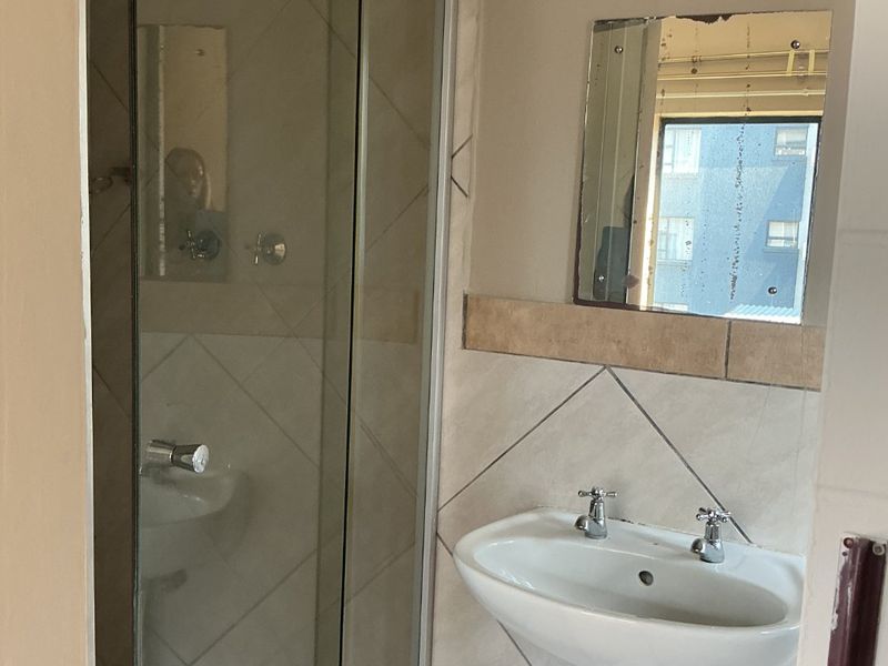 A functional bathroom featuring a pedestal basin, a glass-enclosed shower, and neutral wall tiling.