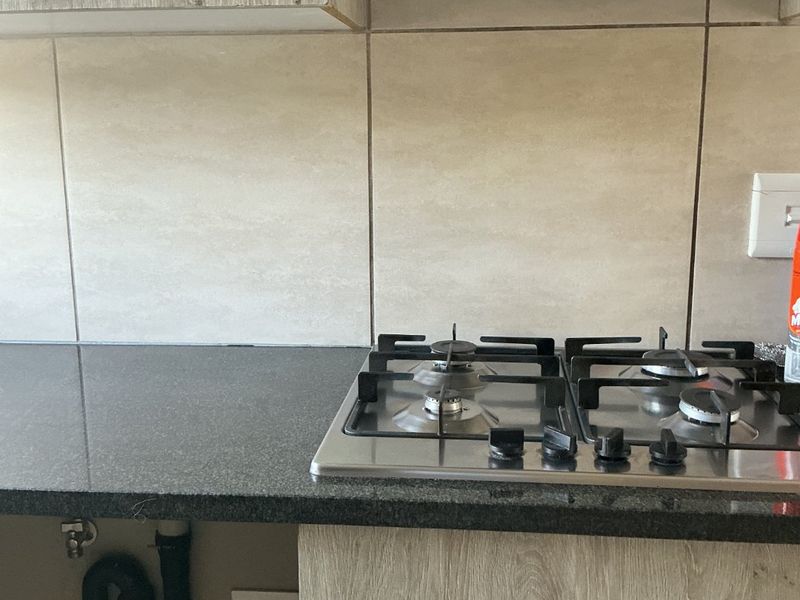 A kitchen area featuring a gas hob, built-in oven, extractor fan, and granite countertops, with visible exposed plumbing and missing cabinetry.