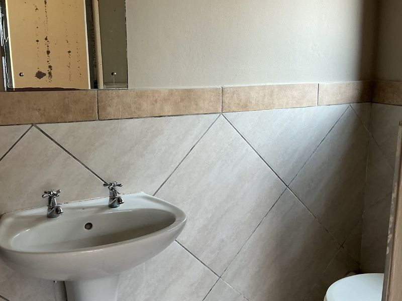 A compact bathroom featuring a pedestal basin, toilet, and neutral ceramic tiling. The space requires minor cosmetic updates to the mirror and finishes.