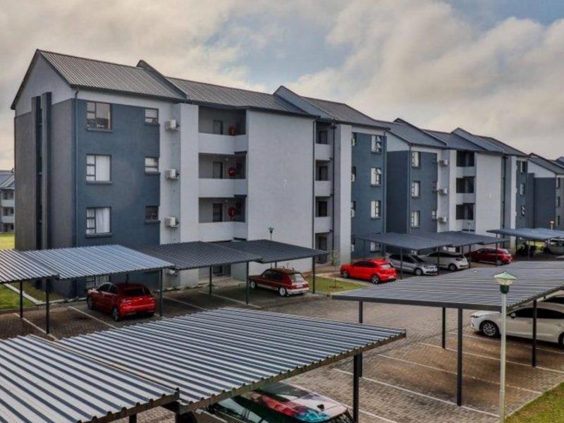 Exterior view of a multi-story apartment complex featuring covered parking bays and paved driveway areas.
