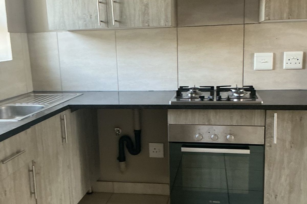 Modern kitchen featuring wood-look cabinetry, built-in oven, gas hob, extractor fan, and tiled finishes. The space is clean and ready for use.