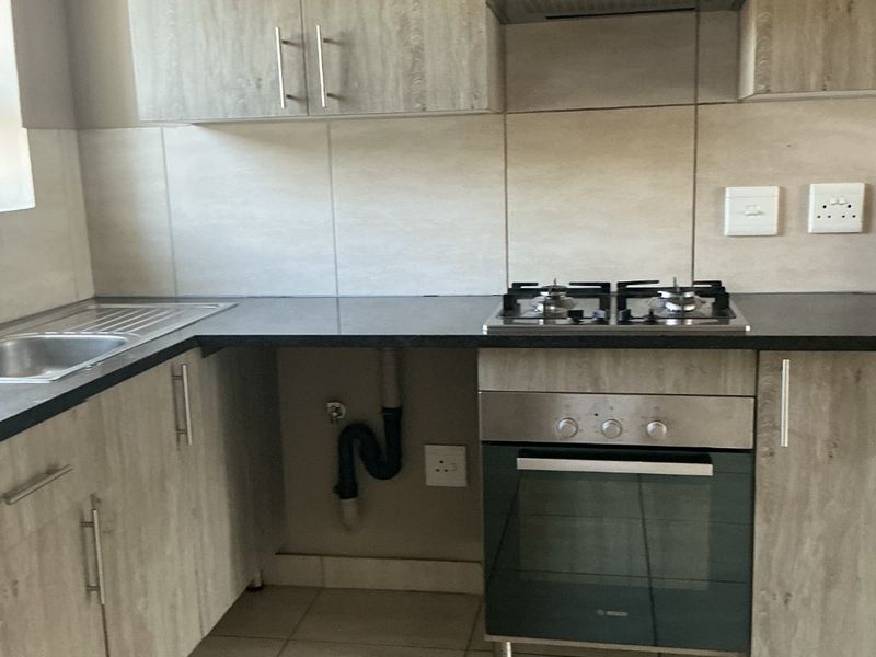 Modern kitchen featuring wood-look cabinetry, built-in oven, gas hob, extractor fan, and tiled finishes. The space is clean and ready for use.