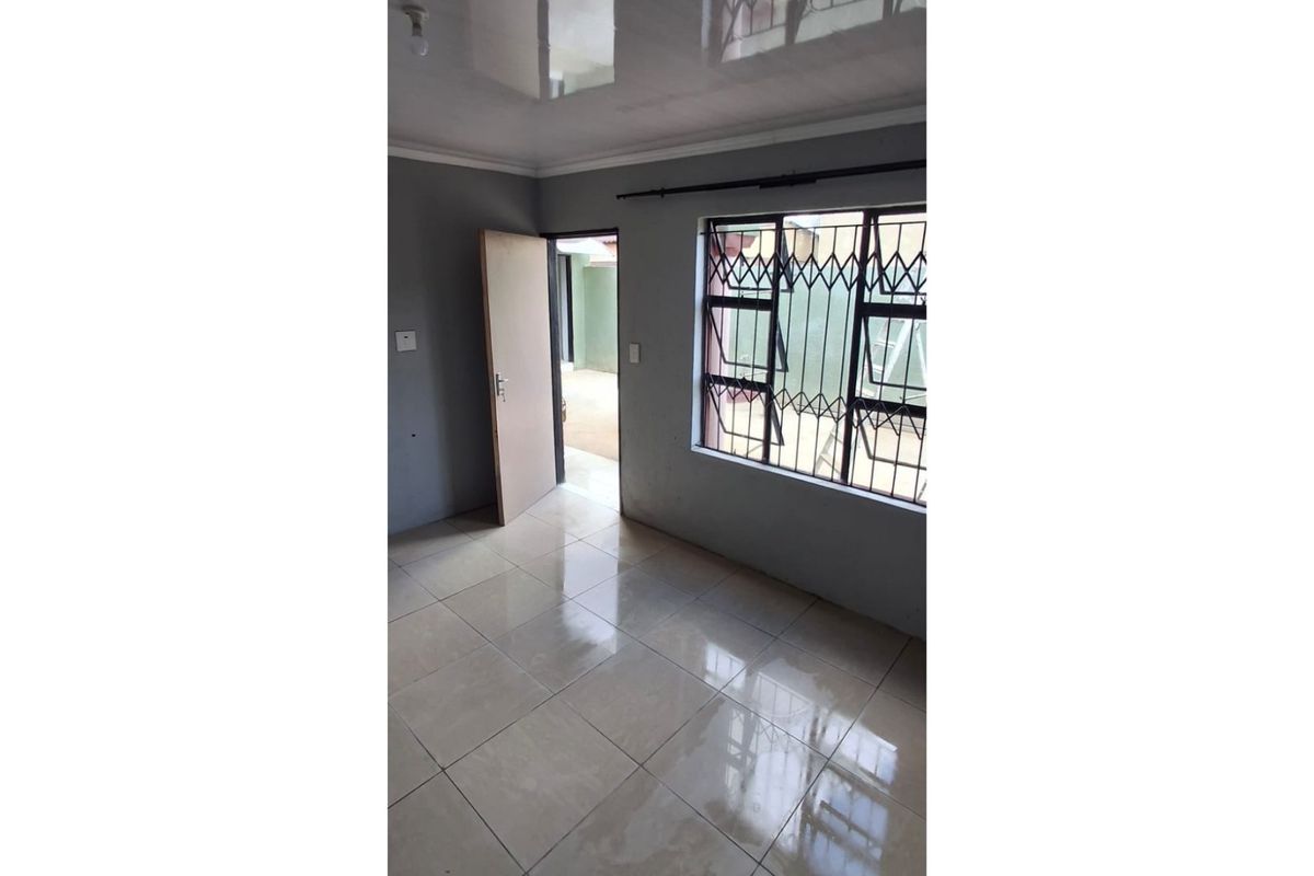 An empty bedroom featuring neutral grey walls, glossy tiled flooring, and a window fitted with a security gate.
