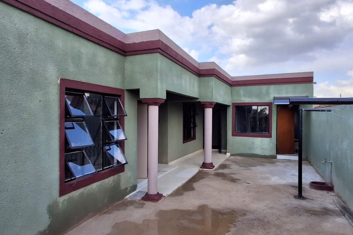 Rear exterior view of the house featuring a concrete patio, covered walkway with structural columns, and top-hung windows.