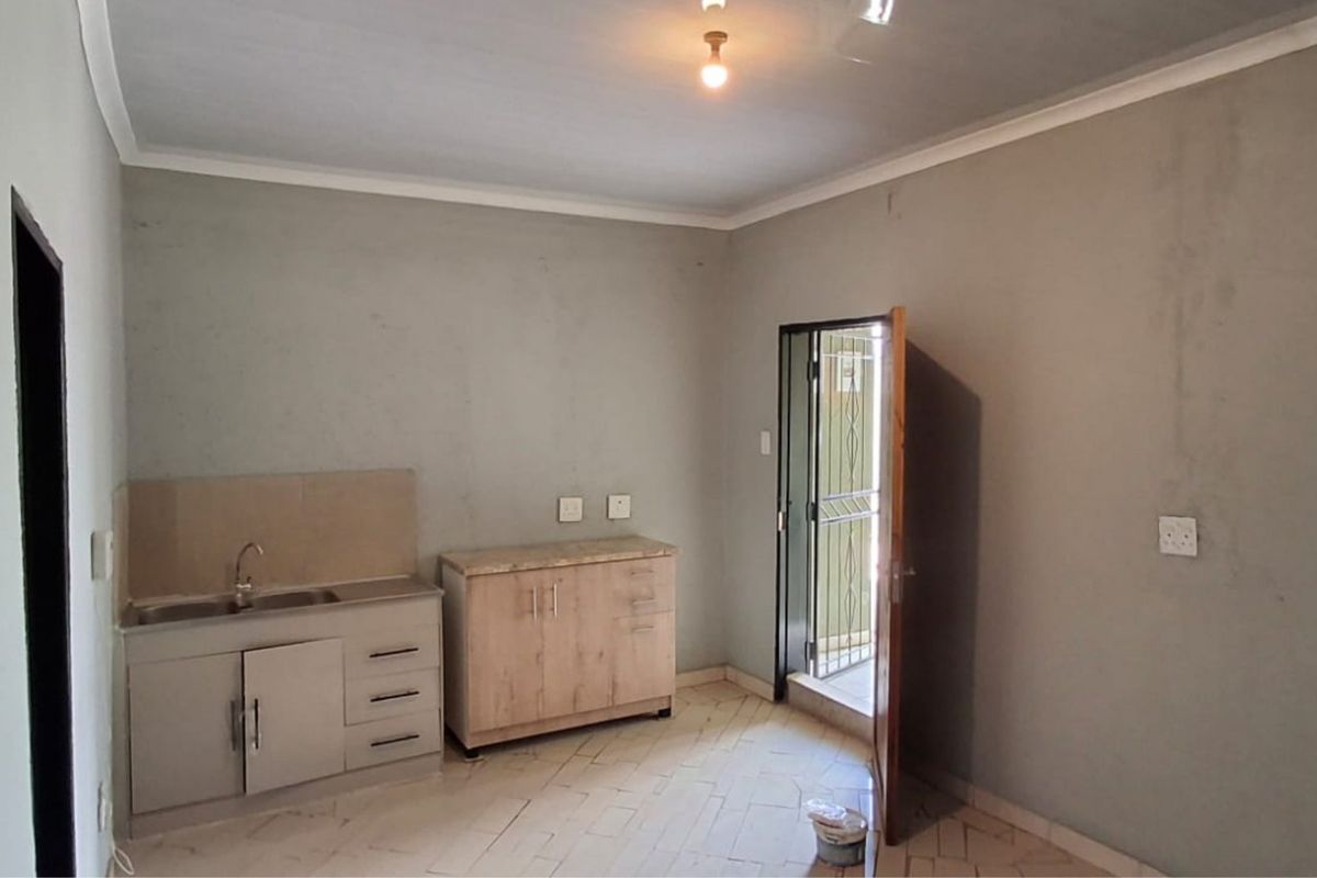 A compact, empty kitchen area featuring basic cabinetry, a stainless steel sink, tiled flooring, and direct access to an exterior doorway.