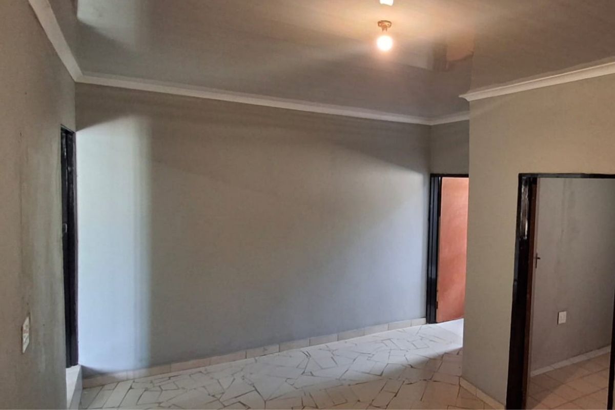 An empty living area featuring tiled flooring, a glossy ceiling, and multiple doorways, currently requiring cosmetic updates and finishing touches to the walls.