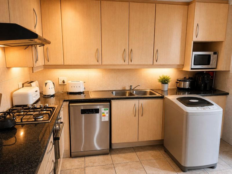 A functional kitchen featuring light wood cabinetry, granite countertops, a gas hob, built-in oven, and integrated space for laundry and dishwashing appliances.