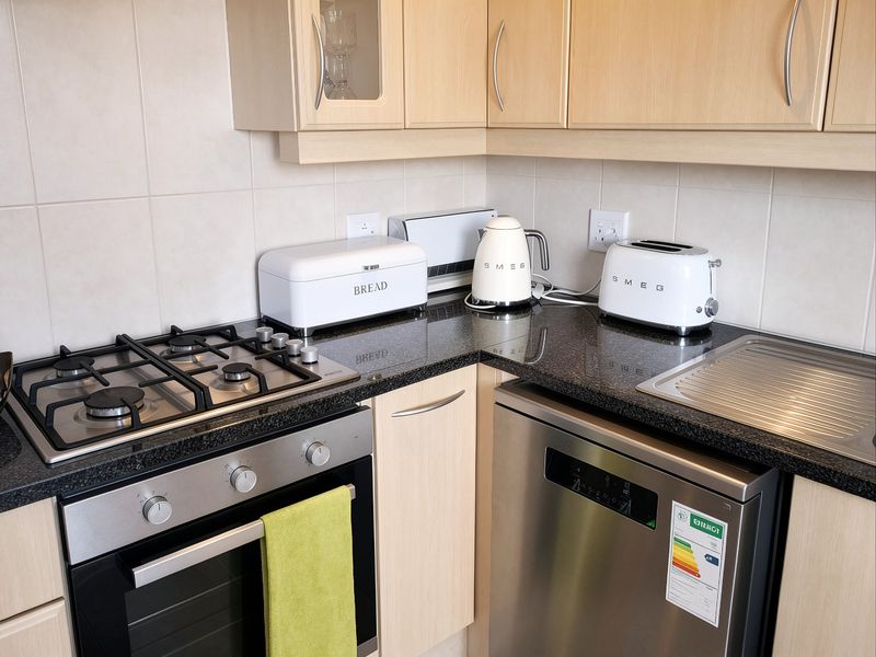 A functional kitchen corner featuring granite countertops, a gas hob, built-in oven, and integrated dishwasher with light wood cabinetry.