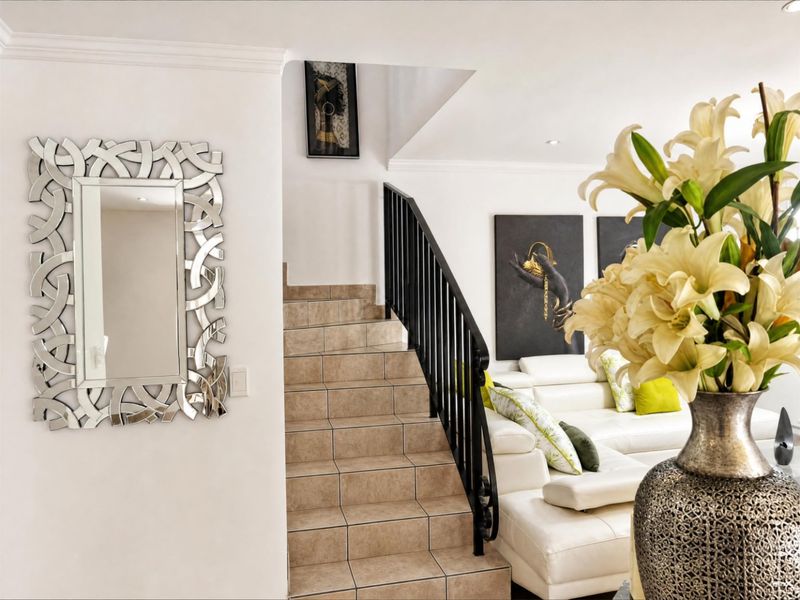 A bright living area featuring a tiled staircase with a decorative wrought iron balustrade, complemented by coving and recessed downlighting.