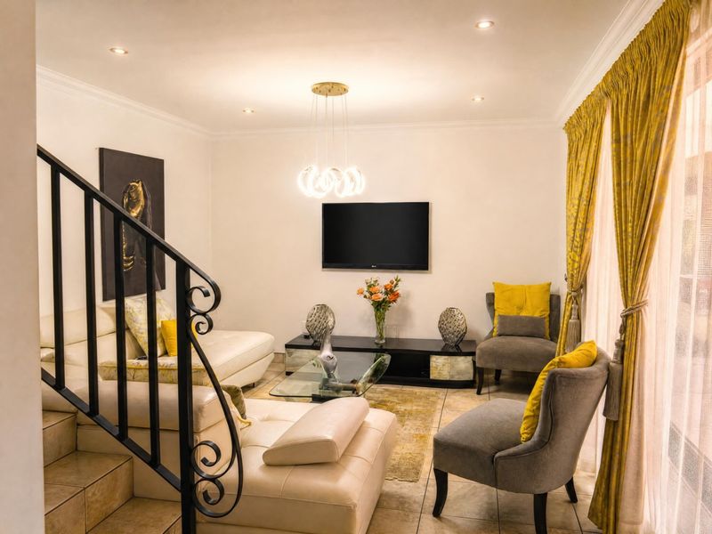 A well-maintained living room featuring tiled flooring, recessed lighting, a decorative pendant fixture, and a wrought iron staircase railing.