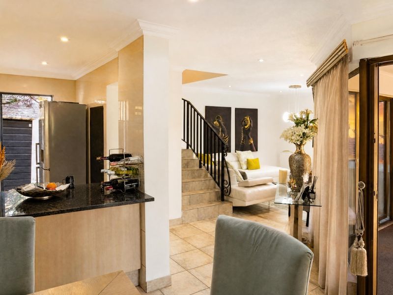 Open-plan living area featuring tiled floors, a granite-topped kitchen counter, and a staircase with a decorative metal balustrade leading to the upper level.