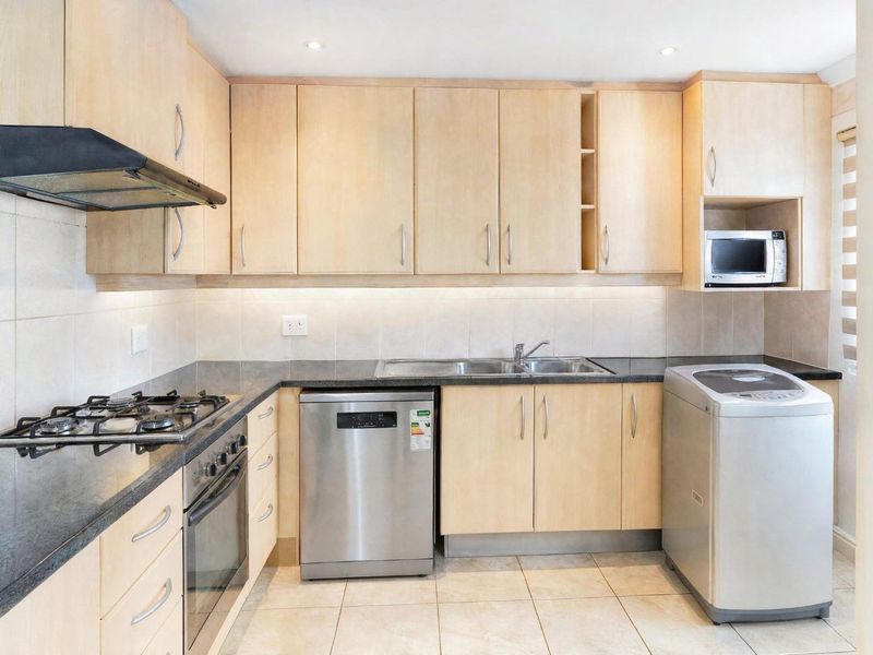 A functional kitchen featuring light wood cabinetry, granite countertops, a gas hob, built-in oven, and integrated space for appliances.
